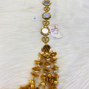 May include: Gold and white beaded tassel with a chain of round mirrors with heart accents. The chain has a small sign with the text "Safa Turban +1-431-405-3060 Follow Us On:  [social media icons]"