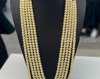May include: A six-strand pearl necklace with gold-toned clasps. The necklace is made of cream-colored pearls and is displayed on a black mannequin.