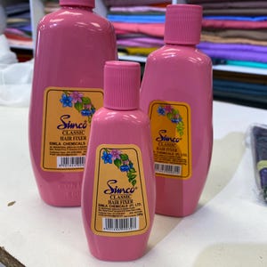 Könnte beinhalten: Drei rosa Plastikflaschen mit Haarfixiermittel. Die Flaschen sind mit "Simco Classic Hair Fixer" und "Simla Chemicals (P) Ltd." beschriftet.