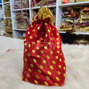 Può includere: Borsa a cordoncino rossa con pois dorati. La borsa è realizzata in un tessuto morbido e setoso e ha una chiusura a cordoncino dorata.