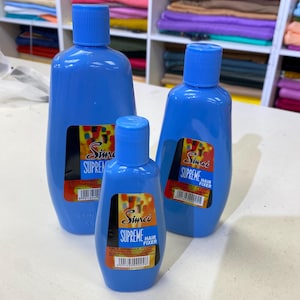 Könnte beinhalten: Drei blaue Plastikflaschen mit Haarfixiermittel. Die Flaschen sind mit "Simco Supreme Hair Fixer" in rot und gelber Schrift beschriftet. Die Flaschen stehen auf einer weißen Oberfläche.