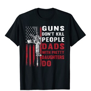 May include: Black t-shirt featuring a distressed American flag design with a rifle graphic. The text reads "GUNS DON'T KILL PEOPLE DADS WITH PRETTY DAUGHTERS DO" in white and red.