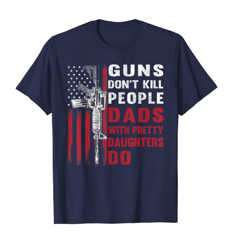 May include: Navy blue t-shirt featuring a distressed American flag design with a rifle graphic. The text reads "GUNS DON'T KILL PEOPLE DADS WITH PRETTY DAUGHTERS DO" in white and red.