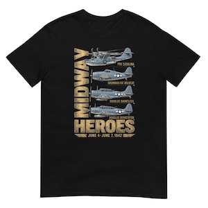 May include: A black short-sleeve t-shirt featuring a graphic of four vintage military aircraft labeled PBY Catalina, Grumman F4F Wildcat, Douglas Dauntless, and Douglas Devastator. The text reads MIDWAY HEROES and JUNE 4-JUNE 7, 1942 in gold.