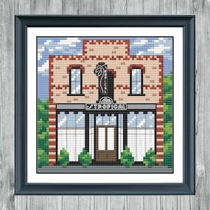 May include: A cross-stitch pattern of a brick building with a sign that reads "La Tropical" and a palm tree logo. The building has two windows on the top floor and a large shopfront with a door and two windows on the bottom floor.