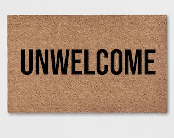 Puede incluir: Una alfombra de bienvenida marrón con la palabra "UNWELCOME" impresa en negro.