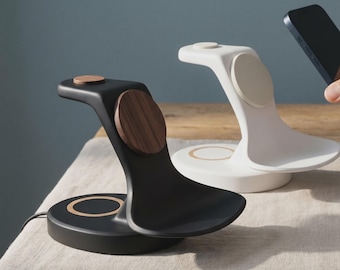 May include: Two wireless charging stands, one matte black and one matte white, each featuring a curved base, a vertical support arm with a circular magnetic charging pad, and a small circular top accent. The black stand has a dark wood grain accent.