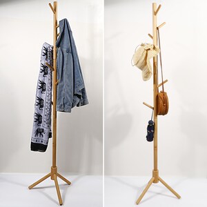 Puede incluir: Un perchero de madera con una base de tr&iacute;pode y m&uacute;ltiples ramas para colgar objetos. Tiene una chaqueta azul, una bufanda con estampado blanco y negro y un sombrero marr&oacute;n colgados.