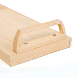 May include: A light wood tray with a handle on the side. The tray has a smooth surface and is made of natural wood. The handle is made of the same wood and has a simple design.