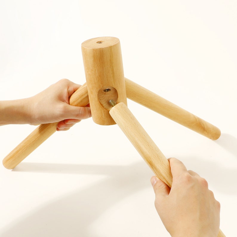 Puede incluir: Un soporte de tr&iacute;pode de madera con tres patas que se est&aacute;n ensamblando. Las patas se est&aacute;n atornillando en la pieza central del soporte.