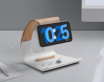 May include: A white wireless charging stand with a wooden base and a phone charging on it. The phone screen displays the time 10:25. There are also a pencil and paper clips on the stand.