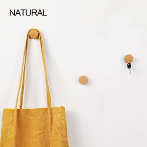 Pode incluir: Três ganchos de parede de madeira com acabamento natural. Uma bolsa de mão amarela está pendurada em um gancho, e uma chave está pendurada em outro gancho.