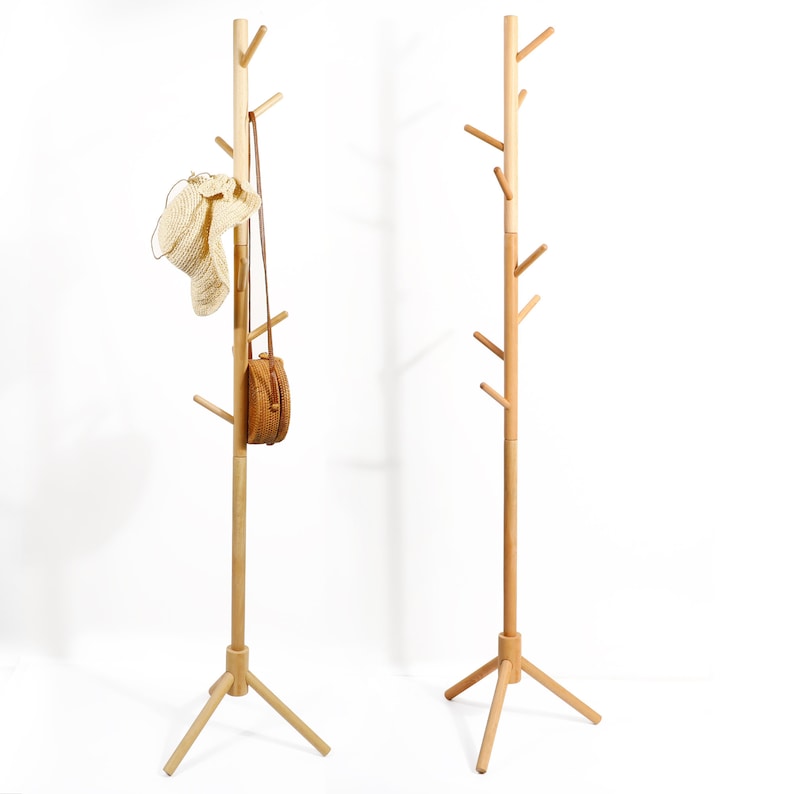 Puede incluir: Dos percheros de madera con un dise&ntilde;o de rama de &aacute;rbol. Cada perchero tiene una base triangular y varias ramas que se extienden para colgar objetos. Un perchero tiene un sombrero de paja y una peque&ntilde;a bolsa tejida colgada de &eacute;l.