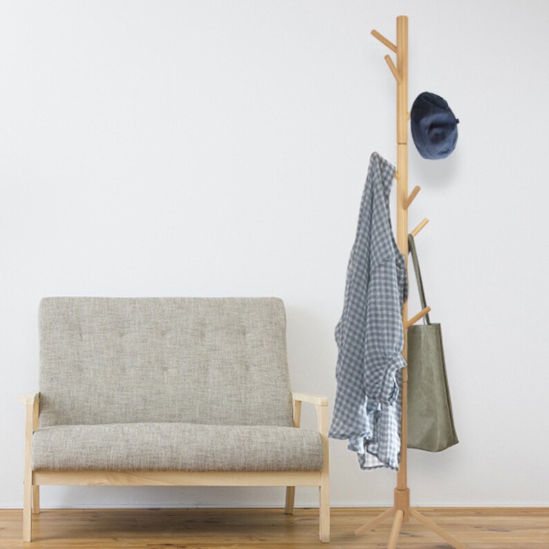 Puede incluir: Un perchero de madera con m&uacute;ltiples ramas para colgar ropa y accesorios. Tiene un acabado de madera natural y est&aacute; de pie sobre un suelo de madera. Un sof&aacute; gris est&aacute; en el fondo.