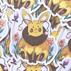Puede incluir: Una pila de pegatinas coloridas con una criatura de dibujos animados similar a una abeja con pelaje amarillo, ojos marrones y una gema púrpura en la cabeza. Las pegatinas están rodeadas de flores y hojas.