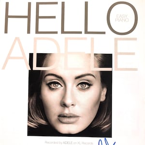Puede incluir: Una portada de libro de música titulada HELLO ADELE EASY PIANO con un retrato en blanco y negro de Adele en el centro. La portada incluye créditos de texto para la canción, una firma en tinta azul en la parte inferior derecha y varios logotipos.