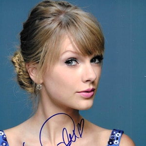 Puede incluir: Un retrato de cerca de una mujer con el pelo rubio recogido en un moño. Lleva un vestido azul con estampado floral y tiene una firma azul en el pecho.