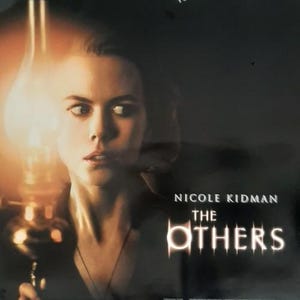 May include: Movie poster for "The Others" featuring Nicole Kidman. The image shows Kidman holding a lantern, with the film's title in a stylized font. The poster has a dark, mysterious atmosphere, with the text "SOONER OR LATER THEY WILL FIND YOU."