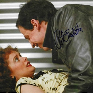 May include: A black and white photo of a man and a woman. The man is wearing a leather jacket and has his arm around the woman. The woman is wearing a white and black patterned shirt. The man's signature, "Peter Facinelli", is written in blue ink on the jacket.