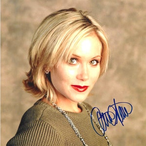 Puede incluir: Una mujer con el pelo corto y rubio que lleva un jersey verde y un collar plateado. Está mirando a la cámara y sonriendo. Su nombre está escrito en tinta azul debajo de ella.