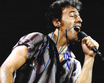 Könnte beinhalten: Signiertes Foto eines Mannes, der auf der Bühne in ein Mikrofon singt. Der Mann trägt ein gestreiftes Hemd mit hochgekrempelten Ärmeln. Das Foto ist mit blauer Tinte signiert.