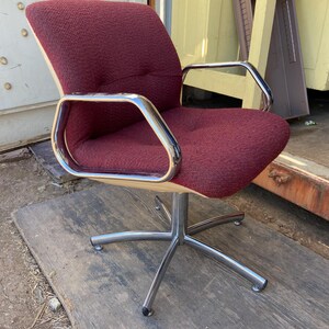 Puede incluir: Una silla de oficina burdeos con estructura cromada y base de cinco estrellas. La silla tiene respaldo y reposabrazos curvos. El asiento y el respaldo est&aacute;n tapizados en tela texturizada. La silla est&aacute; dise&ntilde;ada para la comodidad y el estilo.