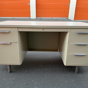 May include: A beige metal desk with three drawers on each side and a center drawer. The desk has a light wood top and silver metal handles.