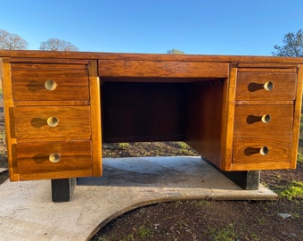 May include: A vintage wooden desk with four drawers on each side. The desk has a dark brown finish and brass drawer pulls. The desk is sitting on black metal legs.