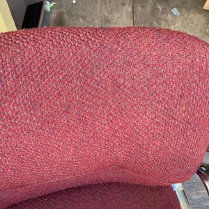 Puede incluir: Primer plano del respaldo de una silla tapizada roja. La tela tiene un aspecto texturizado y tejido. La silla tiene un respaldo curvo y un marco de metal cromado. La silla parece ser vintage.