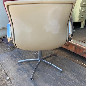 Puede incluir: Una silla de oficina vintage con asiento color crema y respaldo burdeos. La silla tiene una estructura cromada y una base de cinco estrellas. La silla es probablemente de la &eacute;poca moderna de mediados de siglo.