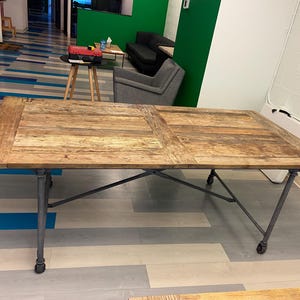 May include: A large rectangular wooden table with a light brown finish. The table has a metal frame with wheels on the legs. The table is approximately 72 inches long and 36 inches wide.