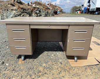 May include: A vintage metal desk with a light brown finish. The desk has a rectangular top and multiple drawers on each side with silver handles. The desk is supported by short, cylindrical legs.