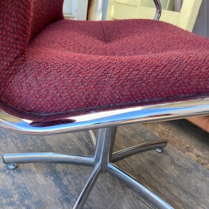 Puede incluir: Una silla moderna de mediados de siglo con un asiento y respaldo texturizados de color burdeos. La silla tiene una estructura de acero cromado y una base de cinco estrellas. La silla est&aacute; dise&ntilde;ada para la comodidad y el estilo.