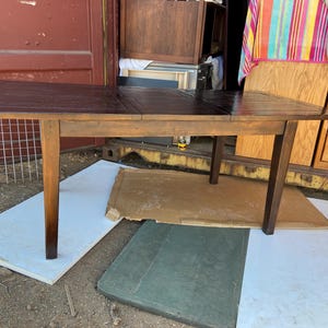 May include: A dark brown wooden table with a rectangular top and four legs. The table is made of wood and has a natural finish. The table is sitting on a white surface.