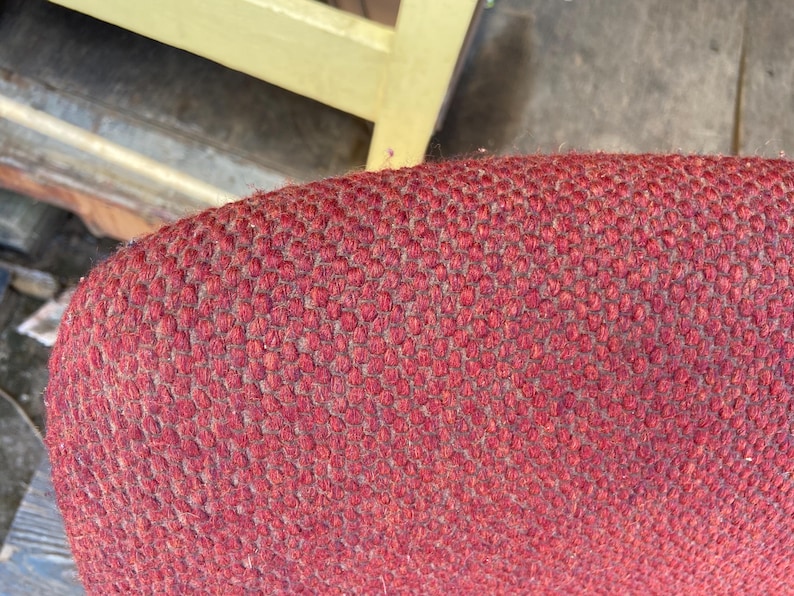 Puede incluir: Primer plano de una secci&oacute;n de tela roja tejida, posiblemente tapicer&iacute;a. La textura es densa con una superficie ligeramente irregular. El color es un rojo intenso y apagado con sutiles variaciones de tono.