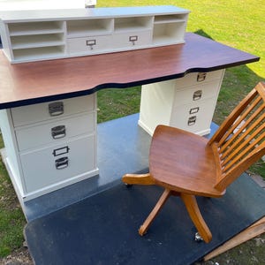 Può includere: Una scrivania in legno con piano marrone scuro e armadietti bianchi. La scrivania ha una credenza abbinata e una sedia in legno con finitura marrone. La scrivania ha cassetti e una credenza con ripiani.