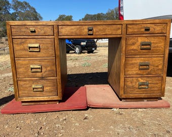 May include: A wooden desk with multiple drawers and brass hardware. The desk has a warm, brown finish and is set on a red mat. The desk has a large open space for a chair and is suitable for a home office.