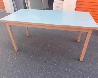 May include: A light brown rectangular table with a light blue top. The table has four legs and is made of metal.