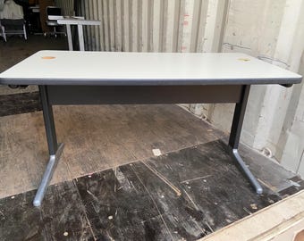 May include: A white rectangular desk with a black metal frame and silver legs. The desk is sitting on a wooden floor.