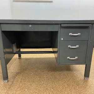 May include: A gray metal desk with three drawers and a single drawer on the left side. The desk has a metal frame and legs.