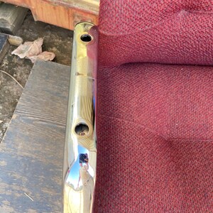 Puede incluir: Un objeto met&aacute;lico cromado brillante con dos agujeros circulares. El objeto est&aacute; posicionado verticalmente, reflejando el entorno. Junto a &eacute;l, una tela burdeos texturizada.