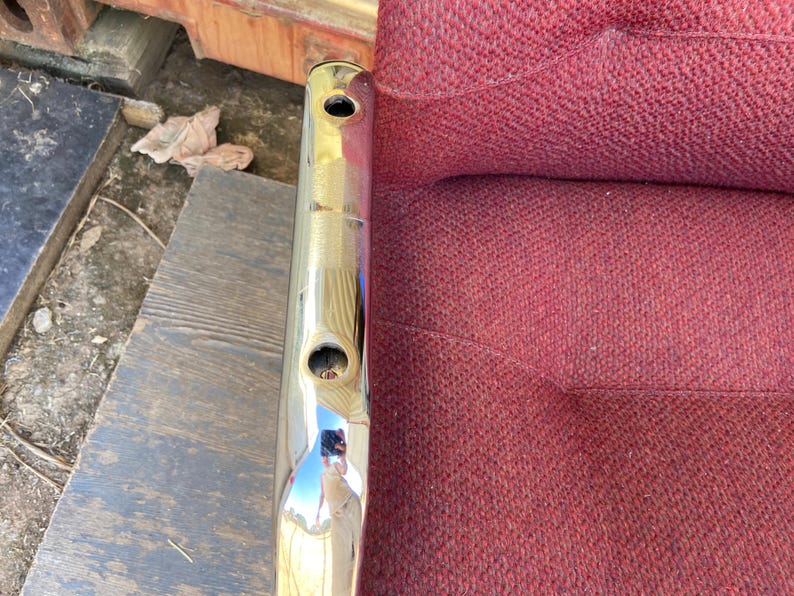 Puede incluir: Un objeto met&aacute;lico cromado brillante con dos agujeros circulares. El objeto est&aacute; posicionado verticalmente, reflejando el entorno. Junto a &eacute;l, una tela burdeos texturizada.