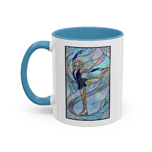 May include: White ceramic mug with a blue handle and interior. The mug features a stained-glass design of a figure skater in a blue and gold outfit, set against a backdrop of swirling blue and white patterns. The design is framed in black.