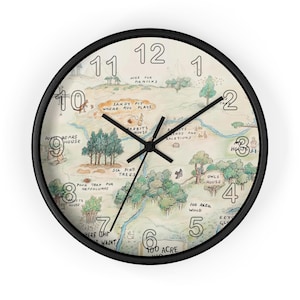 May include: A round wall clock with a black frame featuring a vintage-style map of the Hundred Acre Wood. The clock face displays hand-drawn illustrations of trees, houses, and paths with text labels including Pooh Bear's House and 100 Acre Wood.