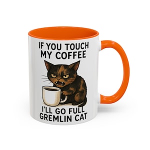 May include: White ceramic coffee mug with an orange interior and handle. The mug features a black cat illustration holding a coffee cup, with the text "IF YOU TOUCH MY COFFEE I'LL GO FULL GREMLIN CAT."