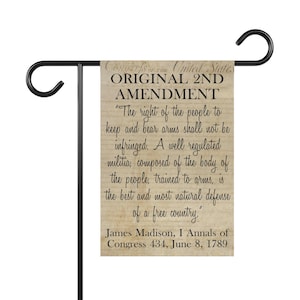 May include: A garden flag featuring the text of the 2nd Amendment of the United States Constitution. The flag has a weathered wood-like background with black text. The flag is attached to a black metal garden stake.