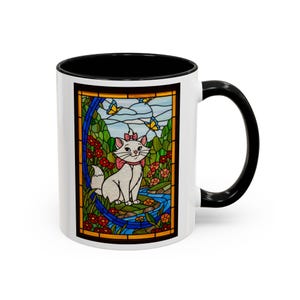 May include: White ceramic mug with a black interior and handle. The mug features a colorful stained-glass style design of a white cat with a pink bow, surrounded by flowers, butterflies, and a stream. The design is framed in a gold border.