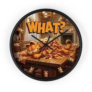May include: A round wall clock with a black frame featuring Garfield lying on a table covered in lasagna. The word "WHAT?" is in orange text above Garfield. Small teddy bear illustrations surround the clock face.