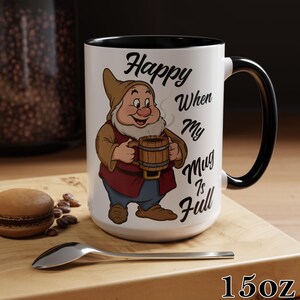 May include: A white ceramic mug with a black interior and handle. The mug features an illustration of a cartoon dwarf holding a wooden mug, with the text "Happy When My Mug Is Full". The mug is 15oz.