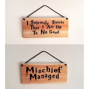 May include: Two wooden signs with black text and a black string for hanging. The top sign reads "I Solemnly Swear That I Am Up To No Good". The bottom sign reads "Mischief Managed".